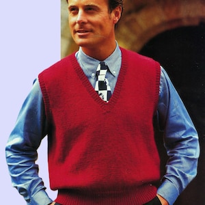 May include: A man wearing a red knitted vest over a blue button-down shirt with a black and white checkered tie.