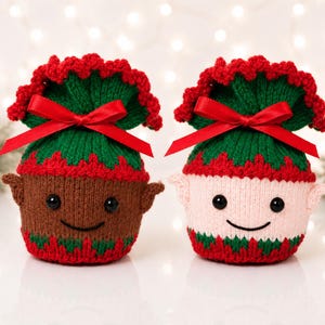 May include: Two knitted elf-themed pouches featuring red, green, and brown or light pink yarn. Each pouch has a red satin ribbon bow, a scalloped top edge, black bead eyes, a stitched smile, and small pointed ears on the sides of the body.