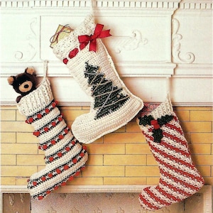 May include: Three crocheted Christmas stockings hanging on a white brick fireplace mantel. The stocking on the left has red and white stripes with red pom-poms. The middle stocking has a green Christmas tree design and a red bow. The stocking on the right has red and white candy cane stripes with a green holly sprig.