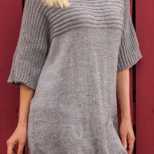 May include: A gray knitted sweater with a loose fit and three-quarter sleeves. The sweater has a ribbed neckline and a slightly longer hem in the back.