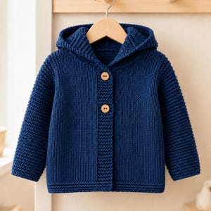 May include: A deep blue knitted hooded cardigan featuring a textured garter stitch pattern throughout the body and sleeves. The garment includes a hood, long sleeves, and a front closure secured by two light brown wooden buttons centered vertically.