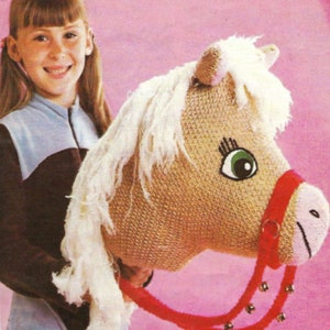 May include: A girl holds a brown and white crocheted stuffed horse with a red bridle and bells. The horse has a green eye and a pink nose.