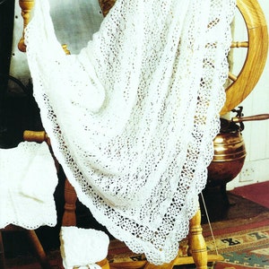May include: A white crocheted baby blanket with a delicate lace border, displayed on a wooden spinning wheel. The blanket is draped over the wheel, showcasing its intricate design.