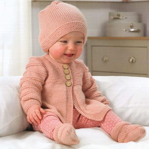 May include: A pink knitted baby cardigan with button fastenings, matching pink knitted hat and pink and white polka dot leggings.