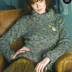 May include: A green, blue and purple knitted jumper with a cowl neck and a decorative pin. The jumper is being worn by a person sitting in a brown leather chair.
