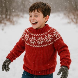 Puede incluir: Un suéter rojo tejido con un diseño de copos de nieve blancos alrededor del cuello. El suéter lo lleva una persona sonriendo y riendo en la nieve. La persona también lleva guantes de color gris oscuro.