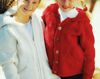 May include: Two girls wearing knitted hooded sweaters. One sweater is white with a zipper closure and the other is red with button closures. Both sweaters have pockets.
