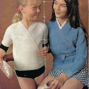 May include: Two girls wearing knitted wrap sweaters. The girl on the left is wearing a white sweater and the girl on the right is wearing a blue sweater. Both sweaters have a V-neck and are tied at the waist.