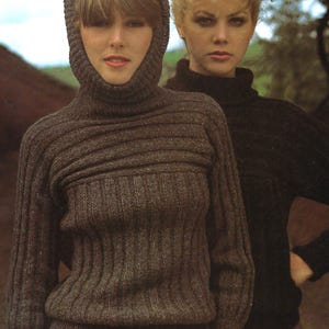 May include: Two women wearing knitted sweaters. One sweater is a dark brown with a hood, and the other is black. The sweaters have a ribbed design. The women are standing outdoors.