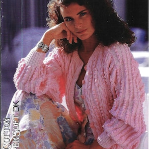 May include: A light pink knitted cardigan with textured sleeves and a button-up front. The cardigan is paired with a floral print dress. The text "Cotton Supersoft DK" is visible on the left side of the image.
