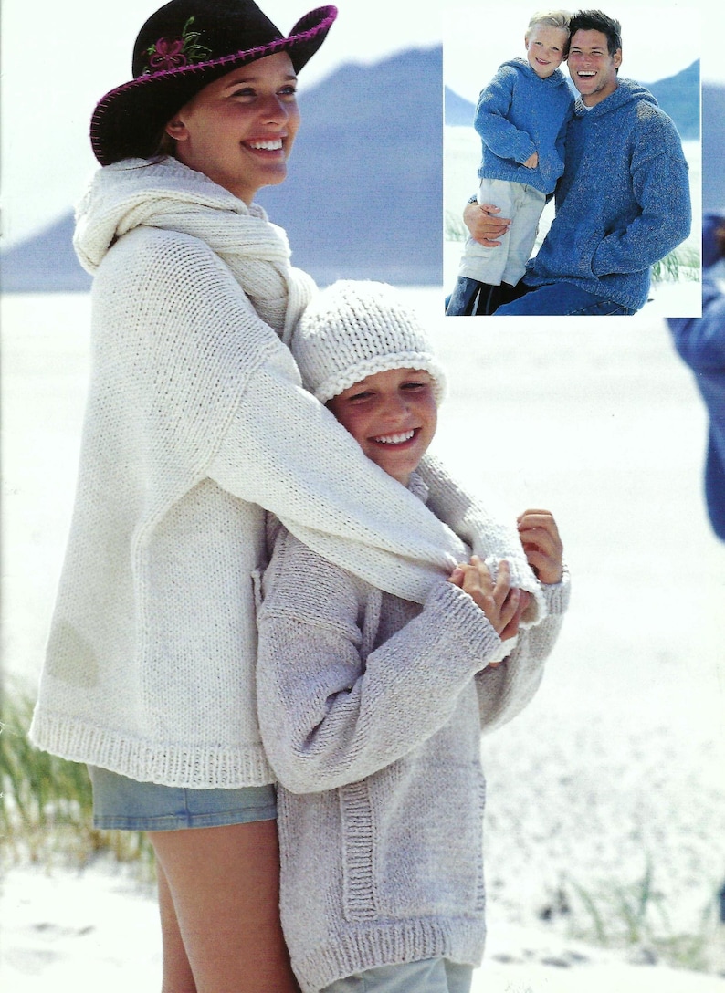 May include: A woman and a child wearing knitted sweaters and hats. The woman is wearing a white sweater with a hood and a black cowboy hat. The child is wearing a light gray sweater and a white beanie. They are standing on a white sandy beach.