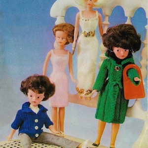 Puede incluir: Cuatro muñecas con ropa de punto. La muñeca de la izquierda lleva una chaqueta de punto azul y pantalones grises. La muñeca del centro lleva un vestido de punto rosa. La muñeca de la derecha lleva un abrigo de punto verde. La muñeca de atrás lleva un vestido de punto blanco con lentejuelas doradas.