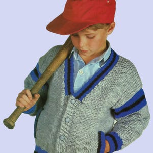 Könnte beinhalten: Ein junges Kind trägt einen grauen Strickpullover mit blauen und schwarzen Streifen, eine rote Baseballkappe und hält einen Holzbaseballschläger.
