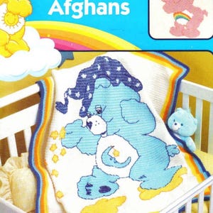 Puede incluir: Un patrón de crochet para una manta de Care Bears con un oso azul Care Bear con una luna creciente y estrellas. El patrón se titula "Care Bears Afghans".
