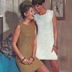 May include: Two women wearing crocheted dresses. The woman on the left is wearing a brown dress and the woman on the right is wearing a white dress. Both dresses are sleeveless and have a crocheted pattern.