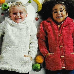 Könnte beinhalten: Zwei Kinder tragen gestrickte Pullover. Das Mädchen trägt einen roten Pullover mit Knöpfen und der Junge trägt einen weißen Pullover mit einer Tasche. Die Kinder sind von Obst umgeben.