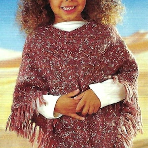 Puede incluir: Una persona joven con un poncho moteado burdeos y blanco con flecos. El poncho se lleva sobre una camiseta blanca de manga larga. El fondo es un cielo azul y un paisaje desértico.