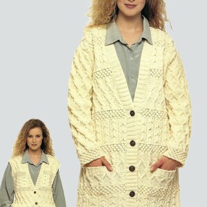 May include: Cream-colored, long-sleeved cardigan with a cable-knit design, button closure, and front pockets. The image also shows a matching cream-colored vest with a button closure. The woman is wearing a light blue collared shirt underneath.