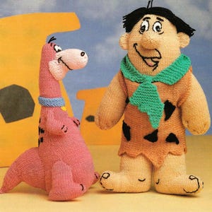 May include: Knitted plush toys of Fred Flintstone and Dino from the cartoon The Flintstones. Fred is wearing a brown loincloth with black spots and a green scarf. Dino is pink and has a blue collar.