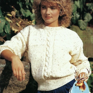 May include: A white knitted jumper with a cable knit design and a speckled texture. The jumper has a round neckline and long sleeves.