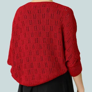 May include: A red knitted bolero sweater with a unique openwork pattern. The short-sleeved sweater is a vibrant red color and has a round neckline. The bolero is made of a soft, textured knit fabric.
