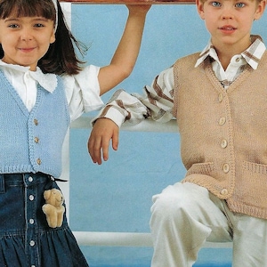 Könnte beinhalten: Zwei Kinder tragen Strickwesten. Das Mädchen trägt eine hellblaue Weste mit Knöpfen und einen Jeansrock. Der Junge trägt eine beige Weste mit Knöpfen und ein weißes Hemd mit Karomuster.