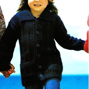 May include: A young person wearing a dark blue knitted cardigan with buttons, a red beret, and blue jeans. The person is walking on a beach.