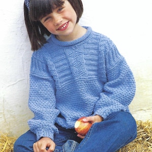May include: A young person wearing a blue knitted jumper with a white headband and blue jeans. They are holding a red apple.