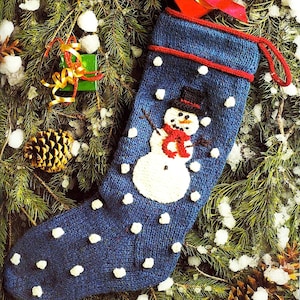 May include: Blue knitted Christmas stocking with a white snowman design and white polka dots. The snowman is wearing a black top hat and a red scarf.