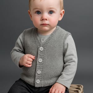 Może przedstawiać: Niemowlę w szarej dzianinowej kamizelce z czterema białymi guzikami na szarej koszulce z długim rękawem. Dziecko ma również na sobie ciemnoszare spodnie. Tło jest w jednolitym szarym kolorze.