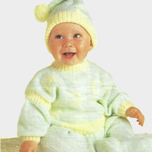 May include: A baby wearing a light blue and yellow knitted sweater and matching hat with a pom-pom. The sweater has a yellow stripe around the neck and wrists.