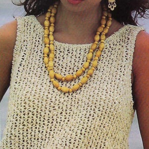 May include: A sleeveless, cream-colored crochet top with a square neckline. The top is paired with a double-strand, light-yellow beaded necklace and matching earrings. The overall style suggests a vintage or bohemian aesthetic.