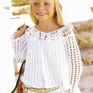 May include: A white crochet top and skirt set. The top has a delicate openwork design with long sleeves. A seashell belt cinches the waist. The outfit is worn by a young person with blonde hair and a headband, carrying a net bag.