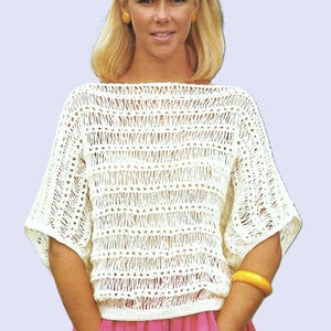 Puede incluir: Un top blanco de ganchillo con un corte holgado y mangas cortas. El top tiene un cuello de barco y un delicado patrón de calado. La modelo lleva una falda rosa y un brazalete amarillo.