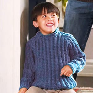 以下が含まれることがあります： 青いニットのセーターを着た若い男の子。セーターはリブ編みで、クルーネックと長袖です。