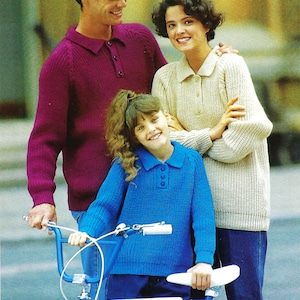 May include: A family poses with a blue bicycle. The adults wear knitted polo shirts in burgundy and cream, while the child wears a blue knitted polo shirt. All are wearing blue jeans. The bicycle has the word "Raleigh" on it.