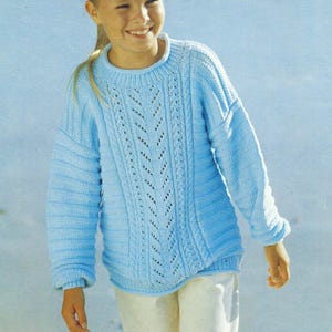 Peut inclure: Un pull en tricot bleu clair avec un motif en câble et une dentelle sur le devant. Le pull a un col rond et des manches longues.