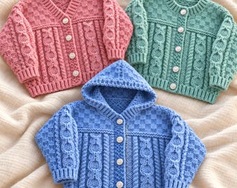 May include: Three knitted cardigans in pink, mint green, and blue. The pink and green cardigans have round necklines, while the blue cardigan features a hood. All garments display a textured cable knit pattern, ribbed cuffs, and white buttons.