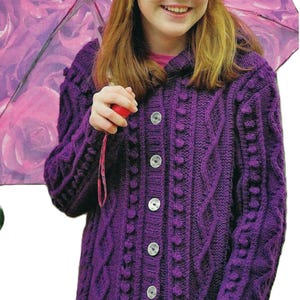 May include: A purple knitted cardigan with a hood, button fastening, and cable knit design. The cardigan has a textured pattern with small round embellishments.