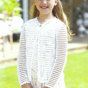 May include: A young girl wearing a white crocheted cardigan with a button closure. The cardigan has a delicate openwork pattern and is worn over a white dress.