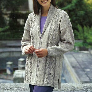 Può includere: Un cardigan a maniche lunghe in maglia a treccia con collo a scialle e chiusura con bottoni. Il cardigan è di colore beige chiaro ed è realizzato in un filato morbido e testurizzato.