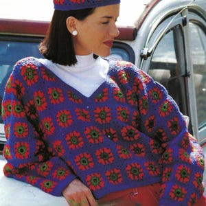 May include: A blue crochet sweater and matching beret with a floral pattern in red and green. The V-neck sweater is paired with red pants and a white turtleneck. The beret sits atop the head.
