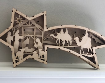 May include: A wooden Christmas star ornament with a nativity scene on one side and the three wise men on camels on the other side.