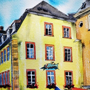 May include: Watercolor painting of a yellow building with red-framed windows and a dark gray roof. A blue fish-shaped sign is mounted on the wall. The sky is a light blue. The building is part of a European town.