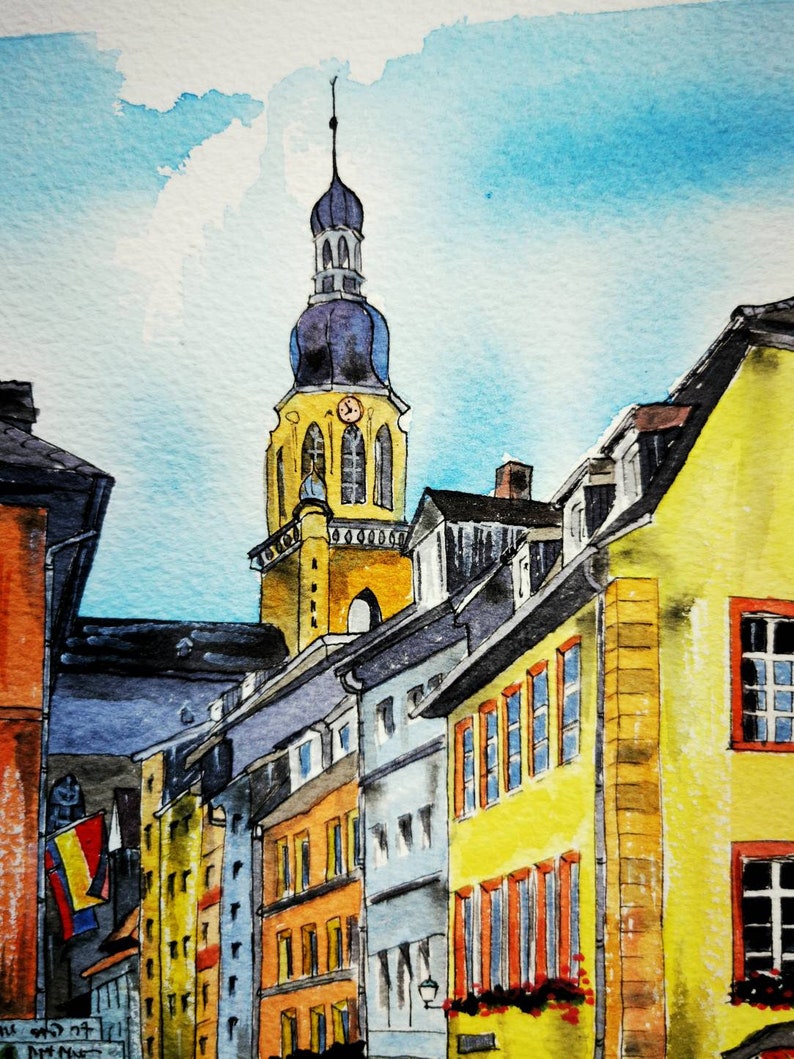 May include: Watercolor painting of a European townscape featuring a tall church steeple with a clock. Buildings in shades of yellow, orange, and blue line the street under a bright blue sky. The artwork captures the architectural details and vibrant colors.