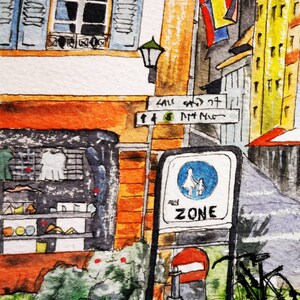 May include: Watercolor painting of a European street scene. Features a storefront, street signs, a bicycle, and a pedestrian zone sign. Buildings are painted in shades of orange, yellow, and blue. The street sign reads "SAU ST" and "ZONE".