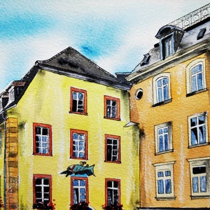 May include: Watercolor painting of European buildings with yellow and orange facades, red-framed windows, and dark gray rooftops. A blue sky is visible above the buildings. The painting style is loose and impressionistic, capturing the essence of the architecture.