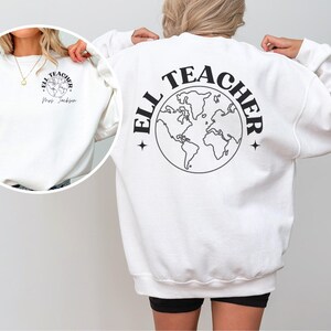 May include: White sweatshirt with a black graphic of a globe with the text "ELL TEACHER" around it. The globe has a star on each side.