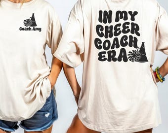 Peut inclure: Deux femmes portant des t-shirts beiges avec du texte noir et un graphique d'un mégaphone et d'une pom-pom de cheerleading. Le texte sur le t-shirt avant dit "Coach Amy". Le texte sur le t-shirt arrière dit "In My Cheer Coach Era".
