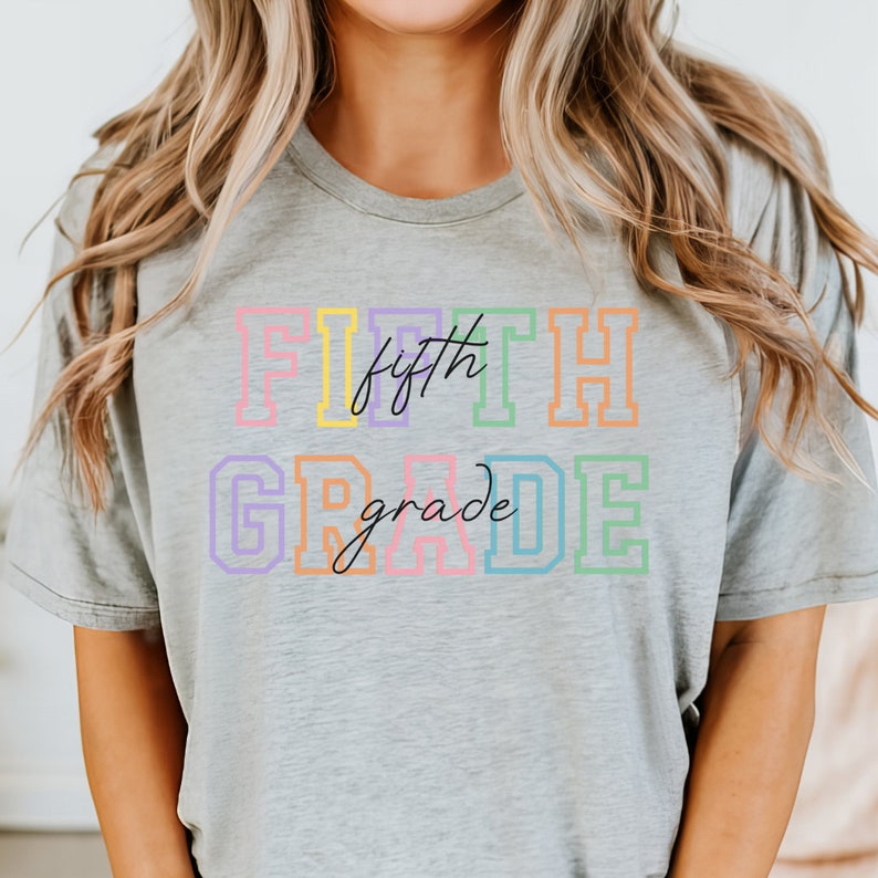 K&ouml;nnte beinhalten: Ein graues T-Shirt mit dem Text "FIFTH grade" in Regenbogenfarben. Das Wort "fifth" ist kursiv geschrieben.